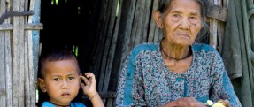 Small child and an old woman sitting in a doorway of a wooden hut